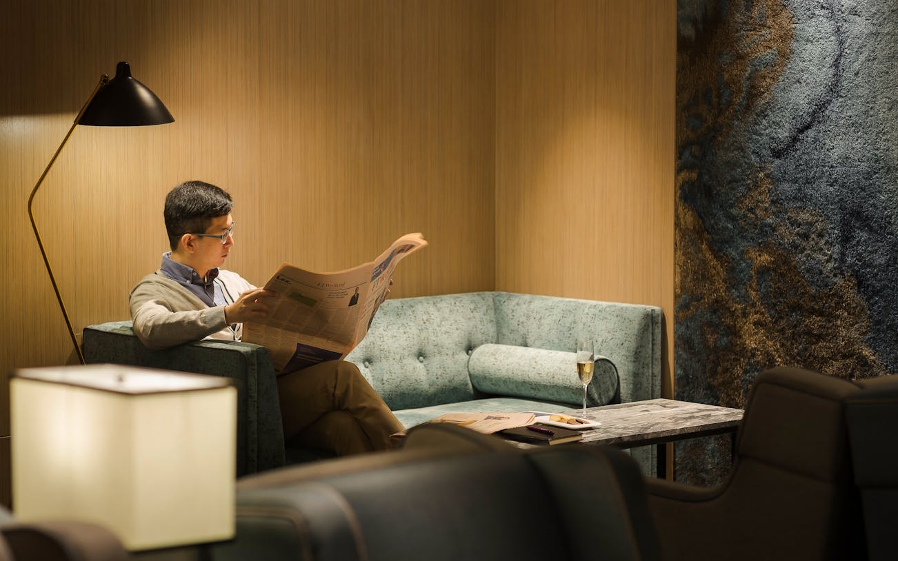 Man reading newspaper in Plaza Premium Lounge, Zone D, Taipei, Taiwan.