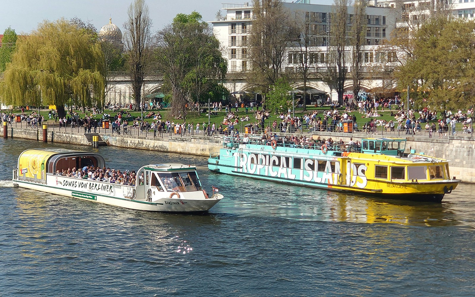 Berlin sightseeing cruise on the Spree River with boats and riverside park.