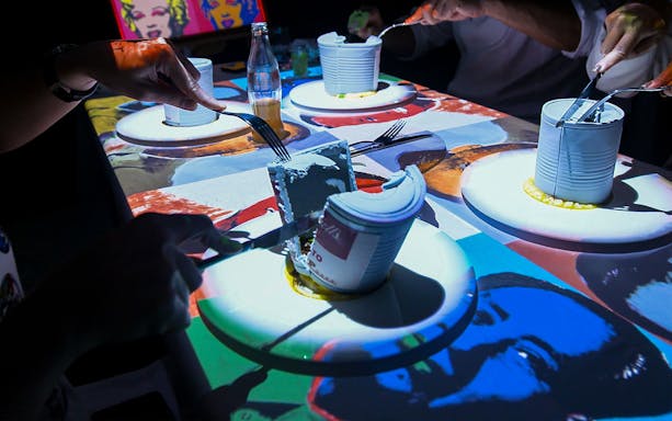 Guests dining at a table with art projections during the Seven Paintings Immersive Dining Show.