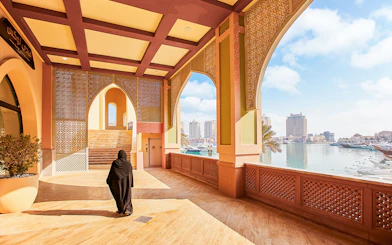 Woman walking through an archway at The Pearl Island, Qatar with marina view.