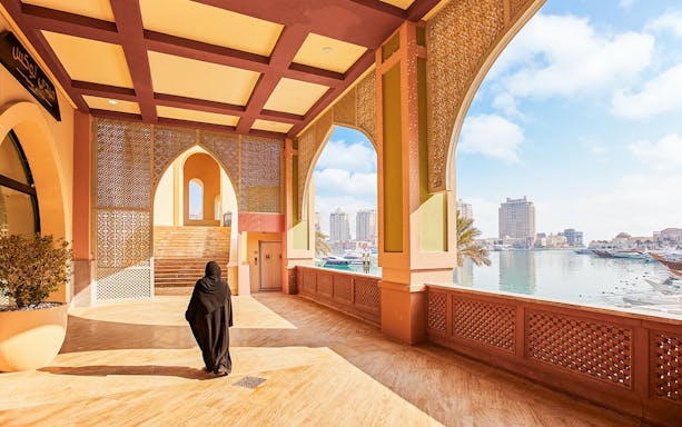 Woman walking through an archway at The Pearl Island, Qatar with marina view.