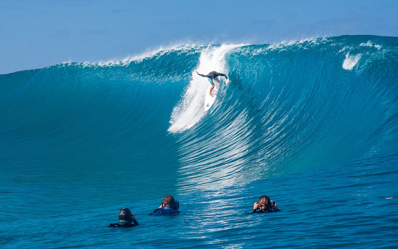 Surfer riding a large wave in Tahiti, French Polynesia, with photographers in the water.