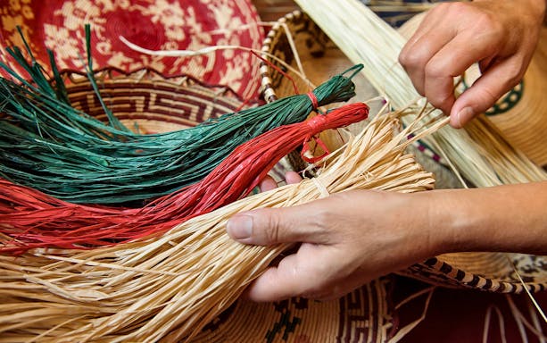 Hands weaving colorful straw in a basket-making workshop.