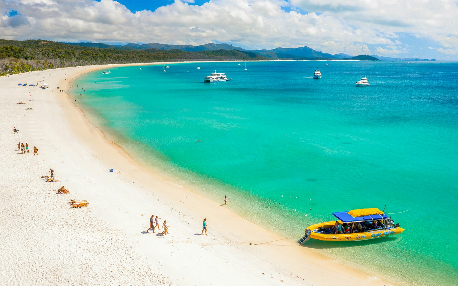 Tourists on Whitehaven Beach, Whitsundays, with a boat anchored near the shore.