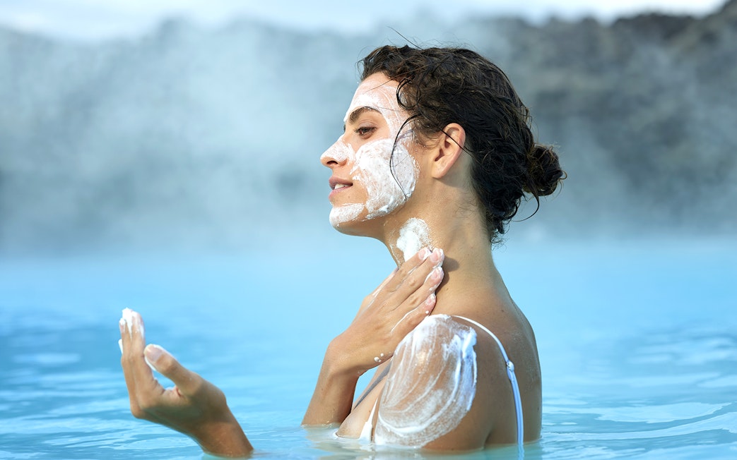 Tourist applying mud mask at Blue Lagoon geothermal pool in Iceland.