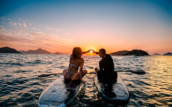 Stand-up paddleboarding at sunrise in Rio de Janeiro, with two people forming a heart shape.