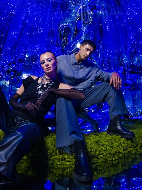 Two people posing in a futuristic, blue-lit room at AYA Universe.