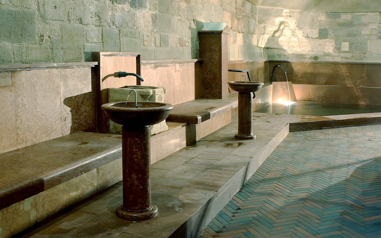 Rudas Thermal Spa interior with stone basins and illuminated pool at night.