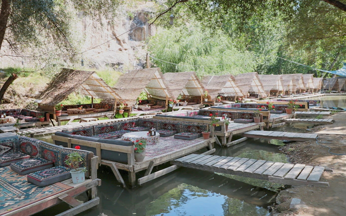Restaurant seating on river in Ihlara Valley, Cappadocia with wooden platforms and woven canopies.