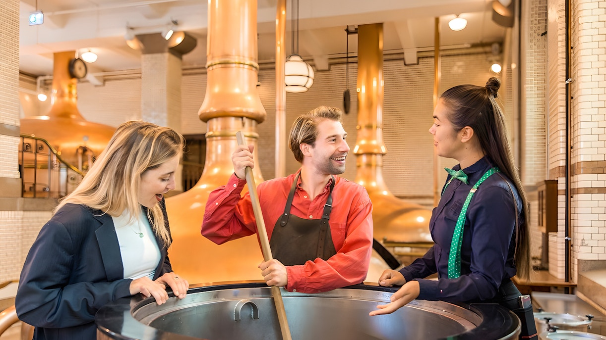 Tourists crafting beer at Heineken Experience in Amsterdam brewery.