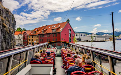 Bergen Hop on Hop off bus with tourists passing colorful waterfront buildings.