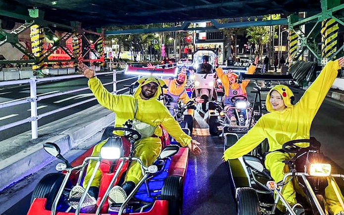 Friends in costumes go-karting at night in a city street.