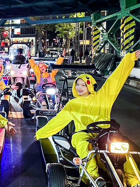 Friends in costumes go-karting at night in a city street.