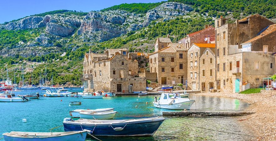 Boats docked by stone buildings on Vis Island, Croatia, with rocky hills in the background.