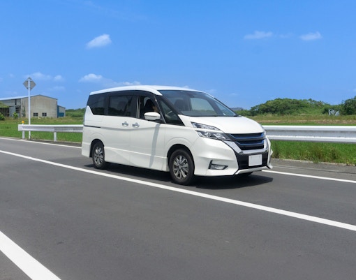 White tour van driving on a highway under a clear blue sky.