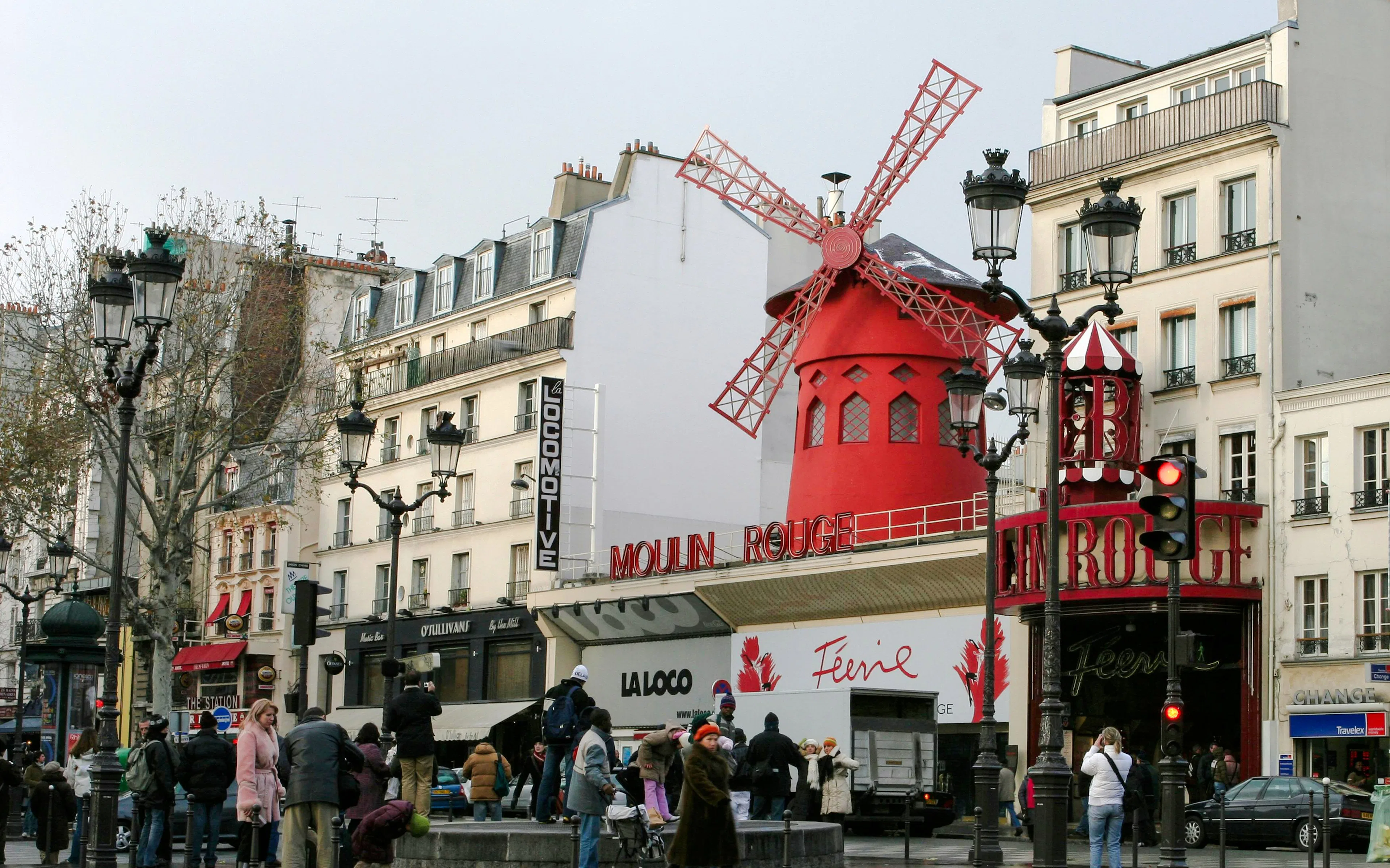 Moulin Rouge red windmill in Pigalle, Paris, with tourists nearby.
