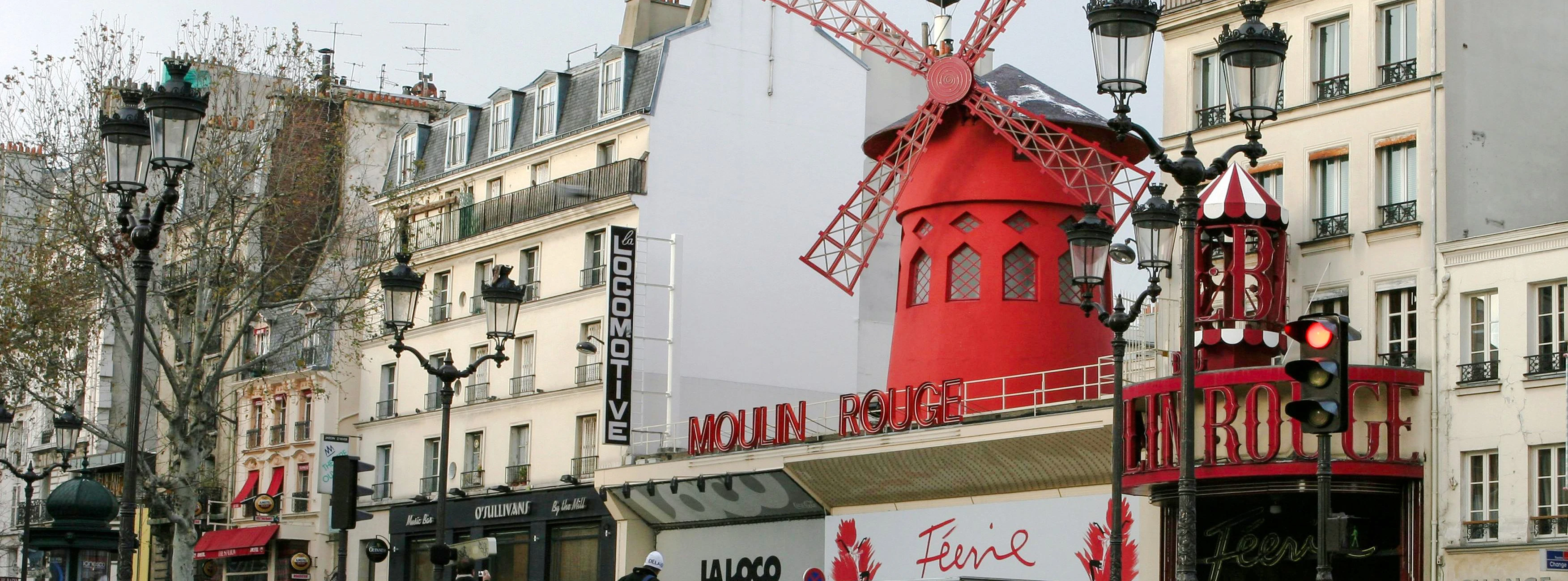 Moulin Rouge red windmill in Pigalle, Paris, with tourists nearby.
