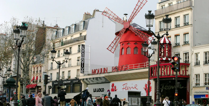 Moulin Rouge red windmill in Pigalle, Paris, with tourists nearby.