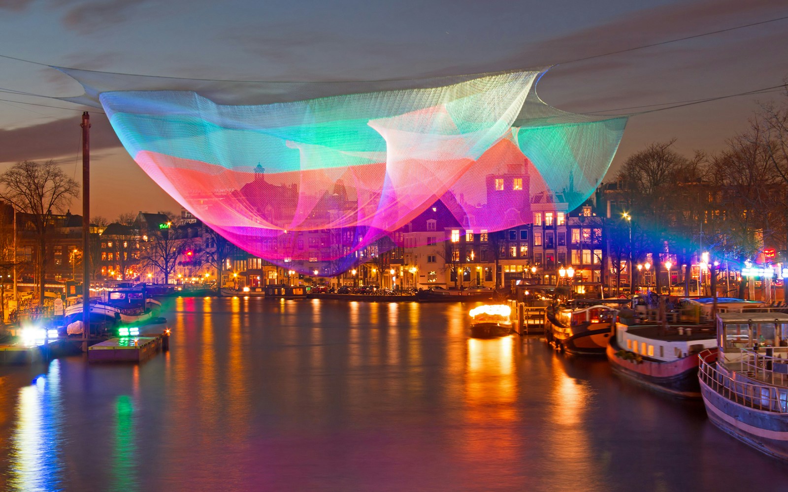 Colorful light installation over Amsterdam canal during the Amsterdam Light Festival.