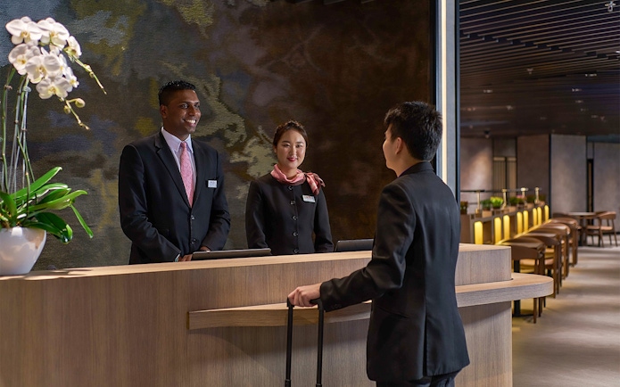 Reception desk at Plaza Premium First, Satellite Terminal, with staff assisting a traveler.