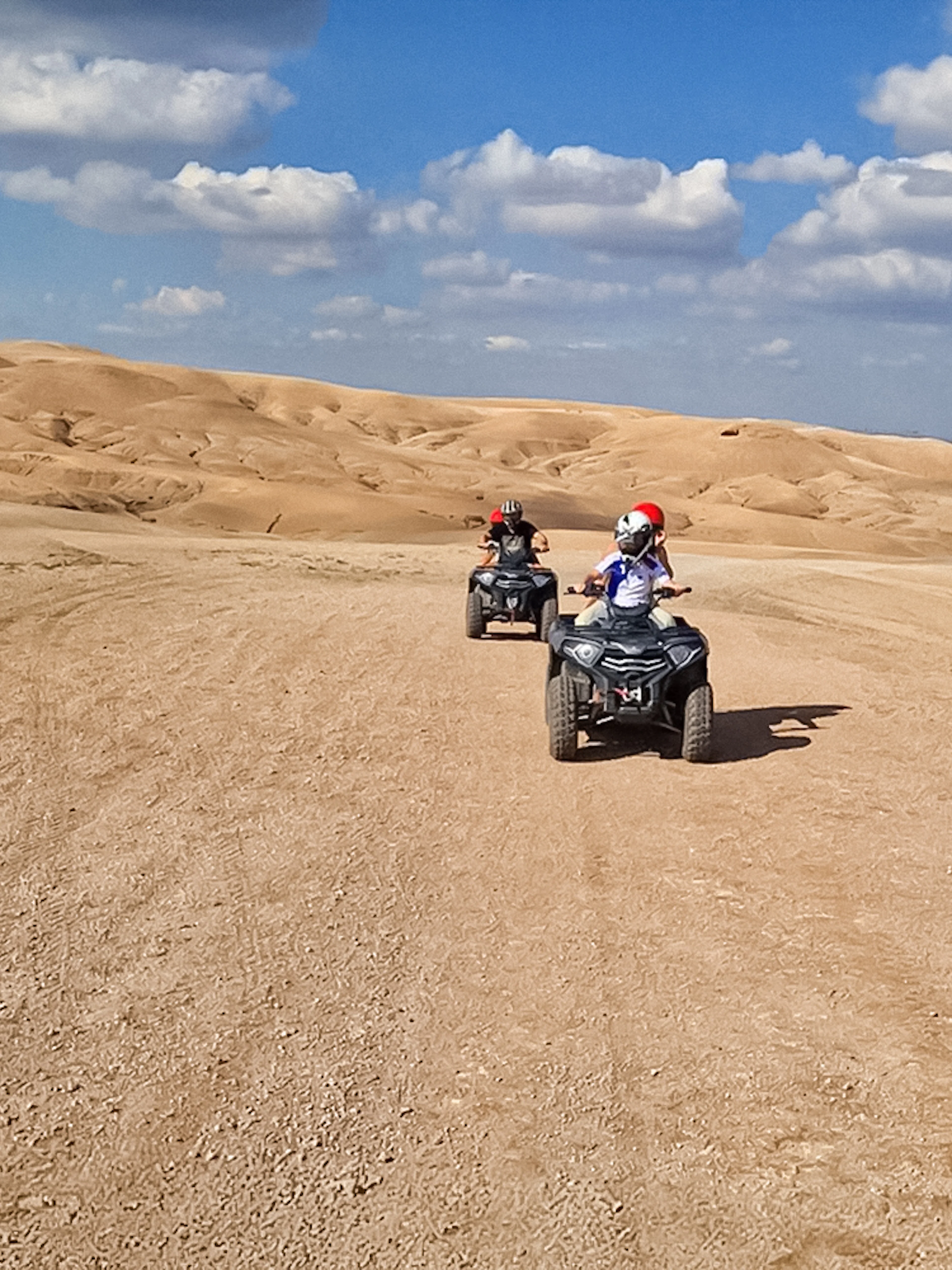 Quad bikers riding through Agafay Desert under a blue sky.