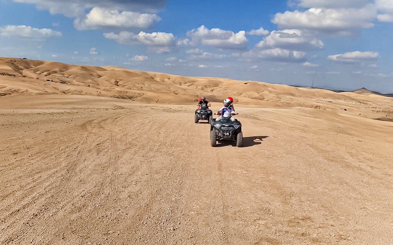 Quad bikers riding through Agafay Desert under a blue sky.