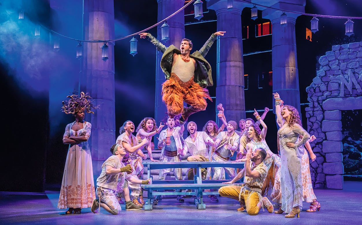 Stage performance of Disney's Hercules with actors in ancient Greek costumes, featuring a lively scene.