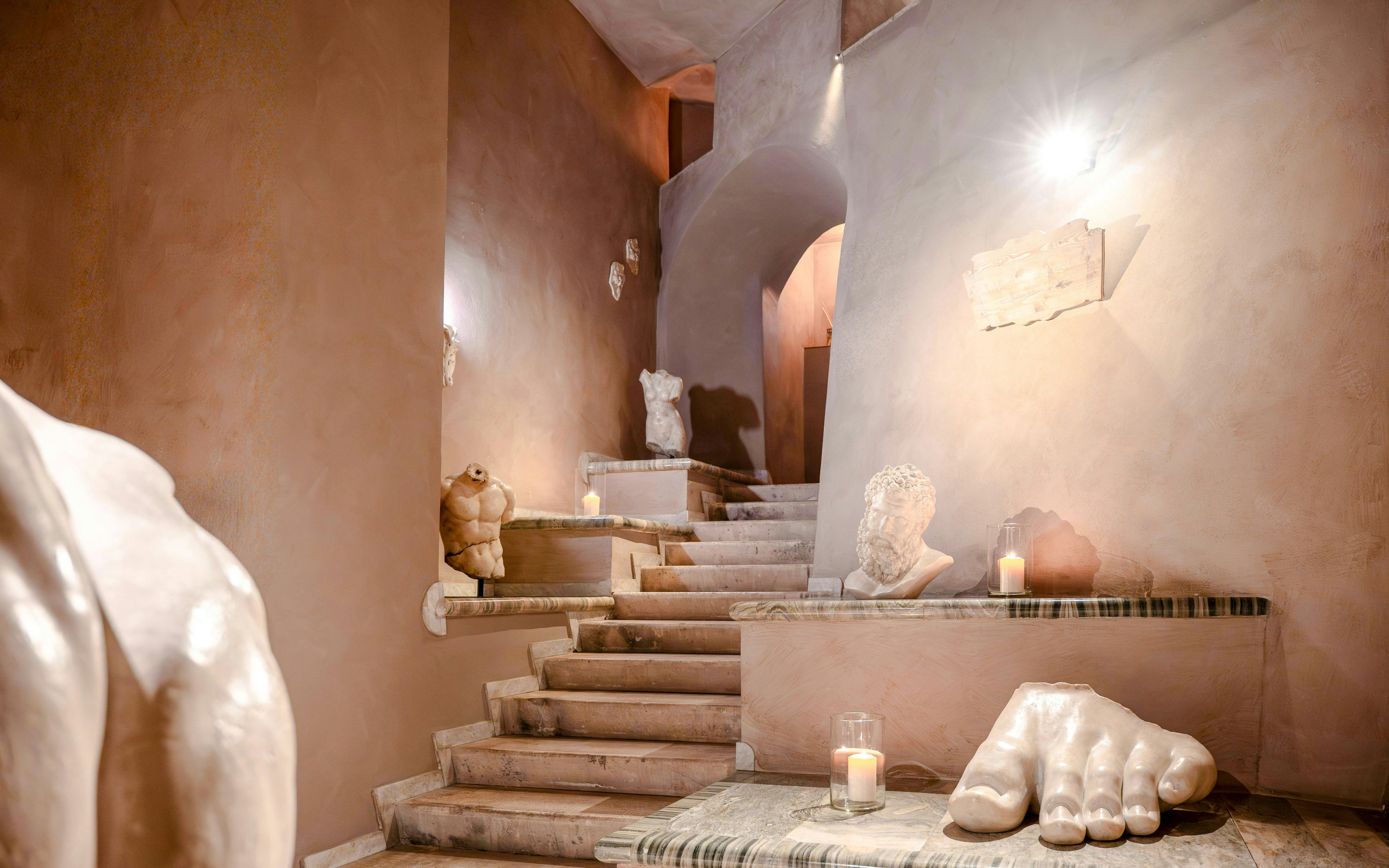 Staircase with classical sculptures and candles at QC Terme Roma spa.