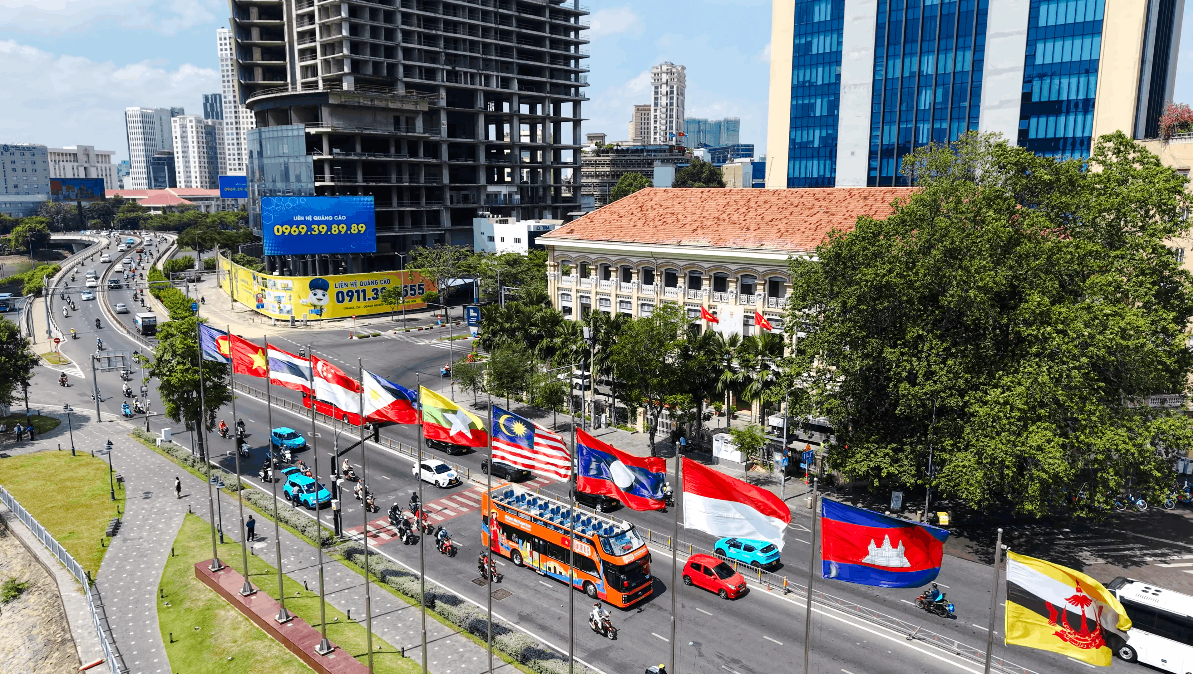Open-top tour bus passing flags on a busy street in Ho Chi Minh City.