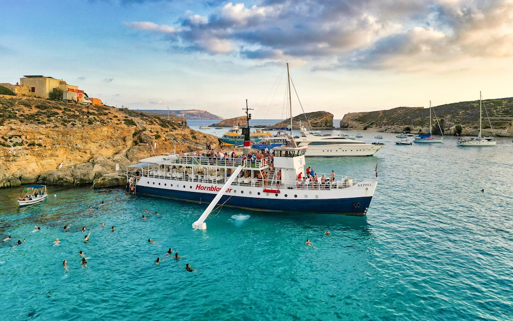 Cruise ship at Blue Lagoon, Malta with swimmers in clear water.