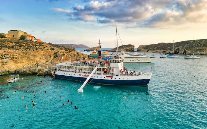 Cruise ship at Blue Lagoon, Malta with swimmers in clear water.