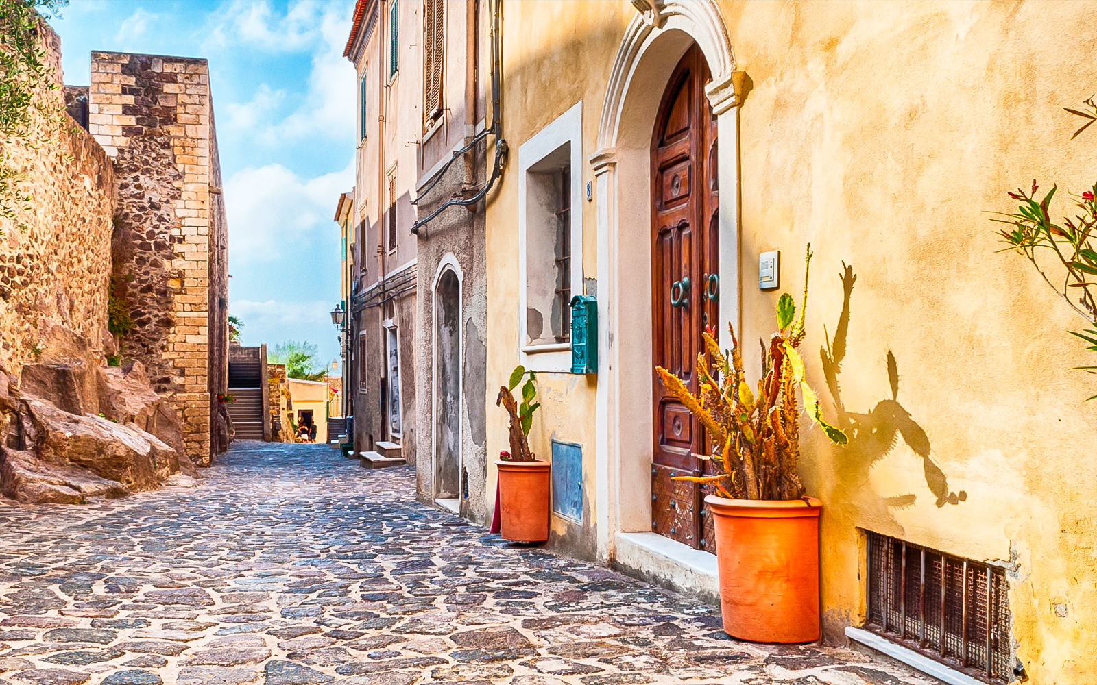 Narrow cobblestone street in Castelsardo with historic buildings and potted plants.