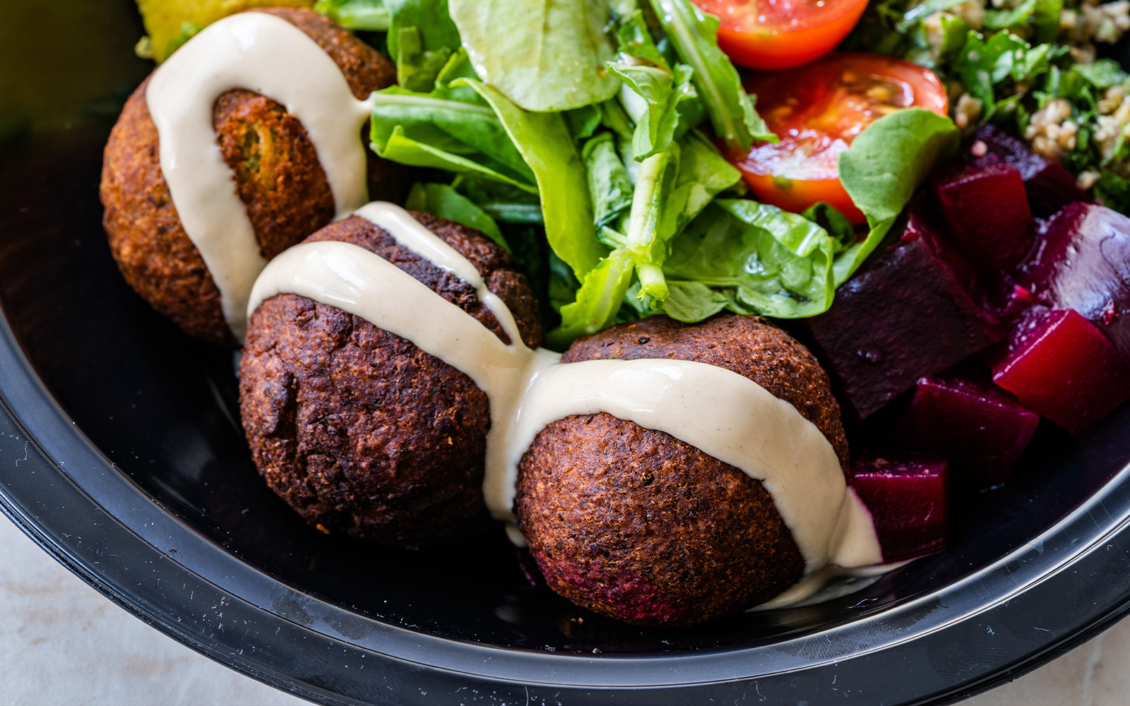 Beetroot falafel bowl with tahini, greens, cherry tomatoes, and diced beets.
