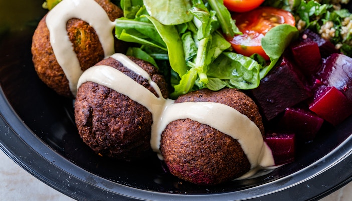 Beetroot falafel bowl with tahini, greens, cherry tomatoes, and diced beets.