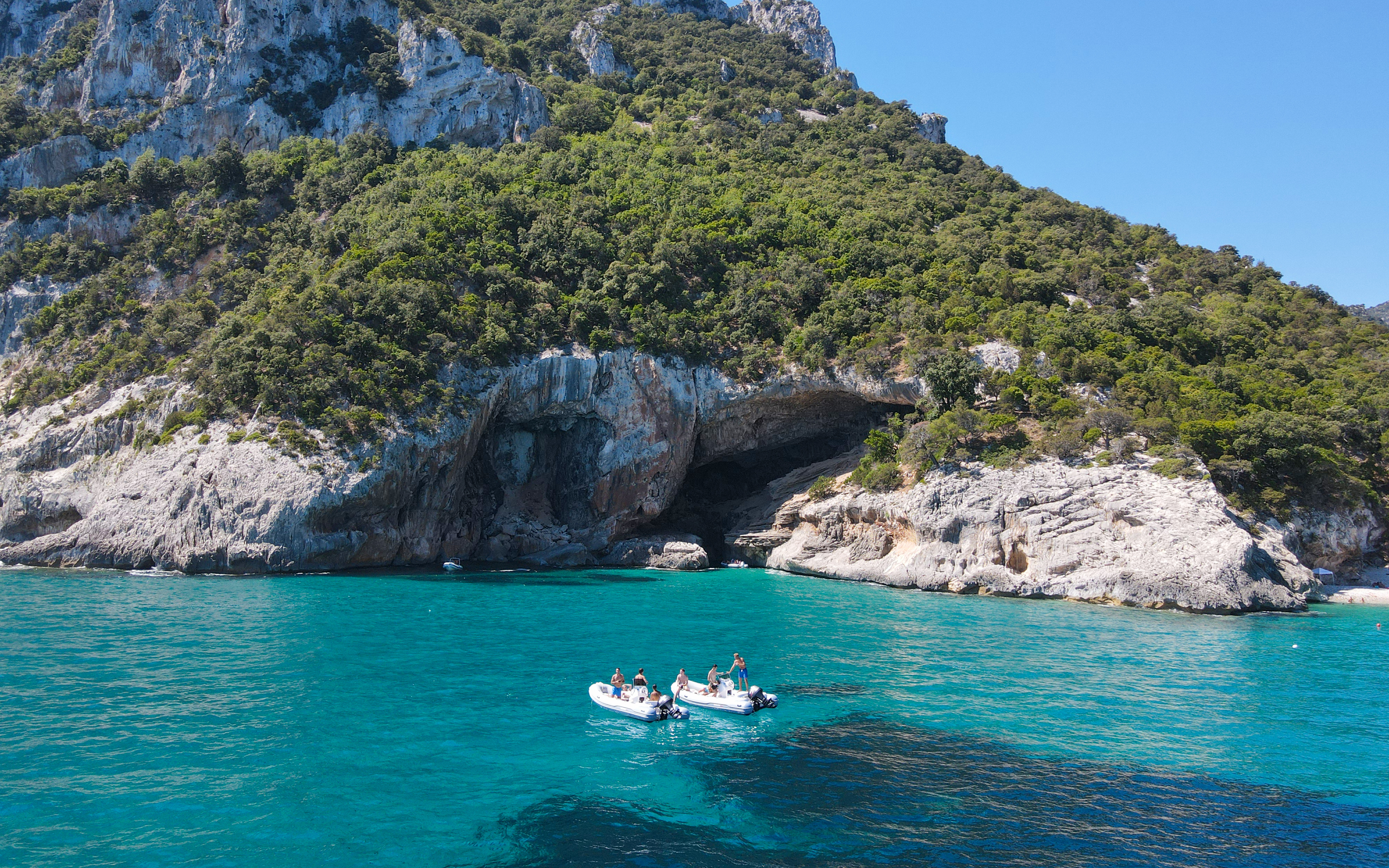 Dinghy on turquoise waters near rocky cliffs at Gulf of Orosei, Dorgali, Sardinia, Italy.