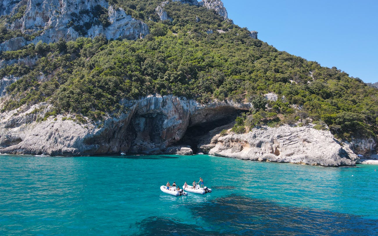 Dinghy on turquoise waters near rocky cliffs at Gulf of Orosei, Dorgali, Sardinia, Italy.