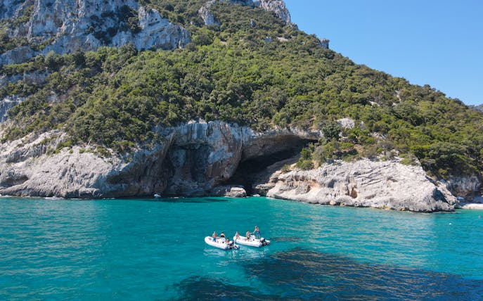Dinghy on turquoise waters near rocky cliffs at Gulf of Orosei, Dorgali, Sardinia, Italy.