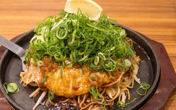 Okonomiyaki topped with green onions and lemon slice on a hot plate.