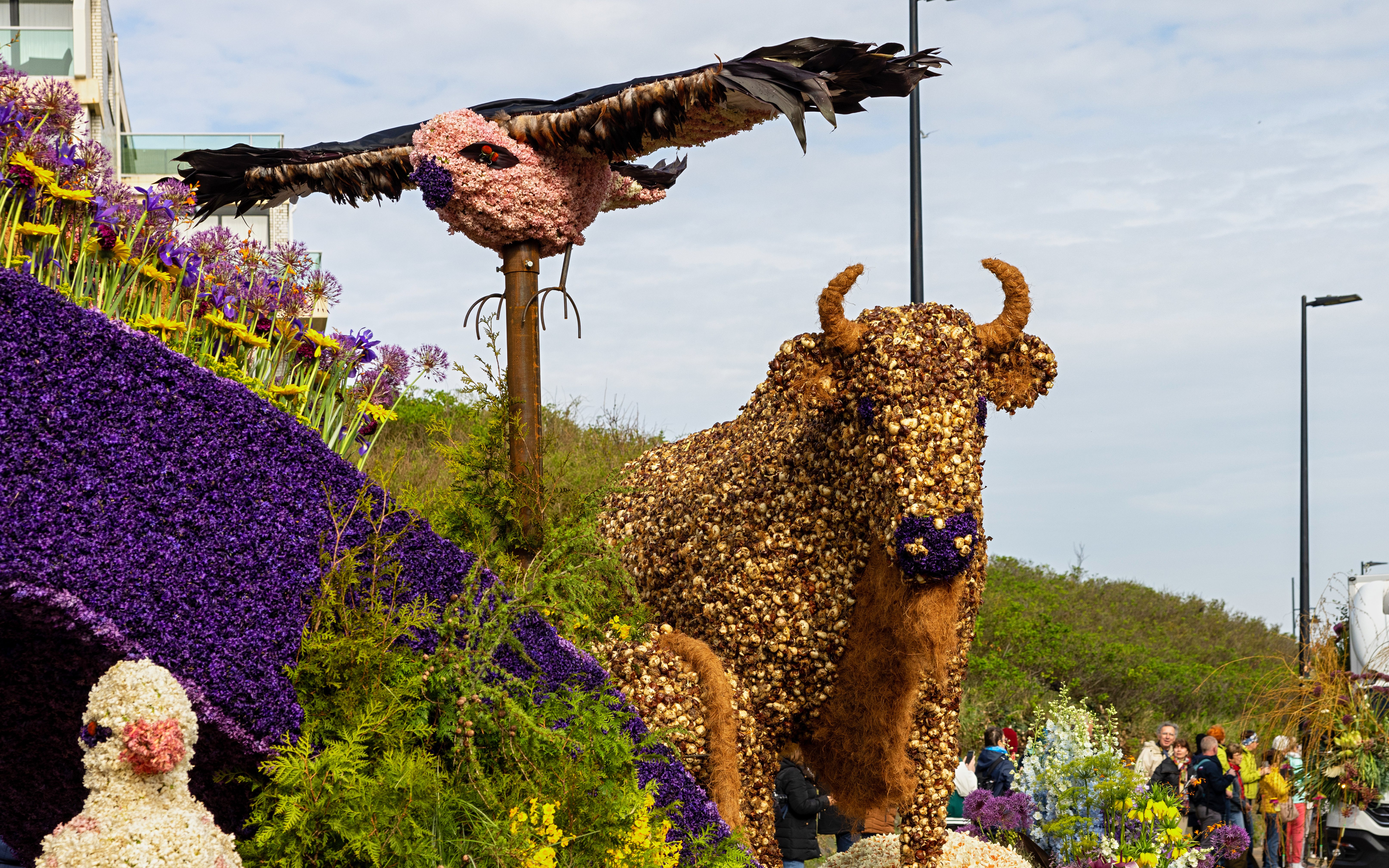 Bull and bird flower installations at a parade with vibrant purple and yellow floral displays.