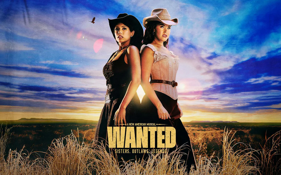 Two women in cowboy hats stand back-to-back in a field under a sunset sky, promoting "Wanted" musical on Broadway.