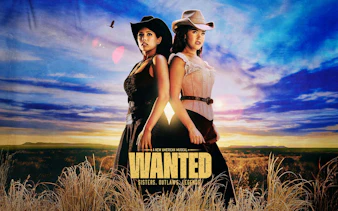 Two women in cowboy hats stand back-to-back in a field under a sunset sky, promoting "Wanted" musical on Broadway.
