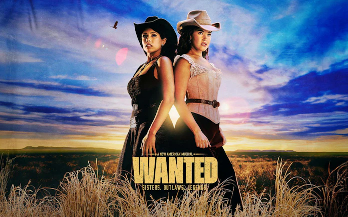 Two women in cowboy hats stand back-to-back in a field under a sunset sky, promoting "Wanted" musical on Broadway.