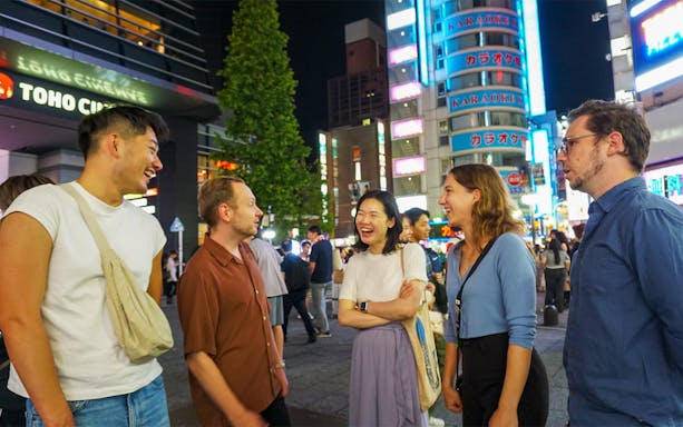 Group enjoying Shinjuku nightlife with neon signs and bustling streets.