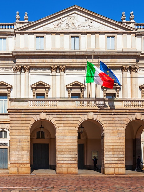 La Scala opera house facade in Milan with Italian and EU flags.