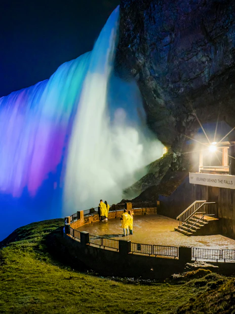 Visitors in yellow raincoats at Journey Behind the Falls, illuminated at night, Niagara Falls.