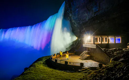Visitors in yellow raincoats at Journey Behind the Falls, illuminated at night, Niagara Falls.