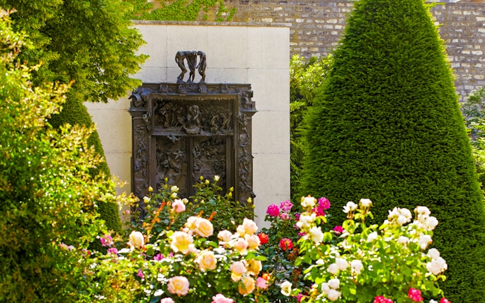 Rodin Museum garden with "The Gates of Hell" sculpture surrounded by flowers and greenery.