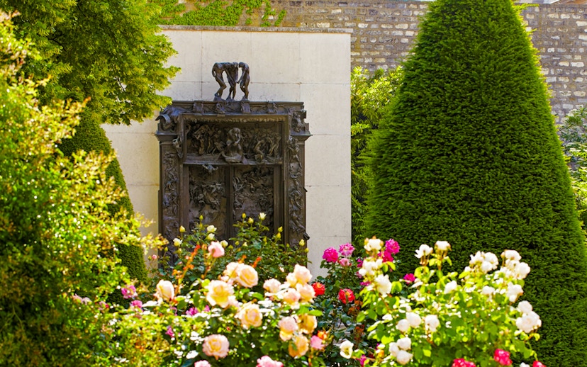 Rodin Museum garden with "The Gates of Hell" sculpture surrounded by flowers and greenery.