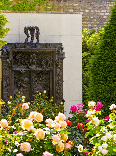 Rodin Museum garden with "The Gates of Hell" sculpture surrounded by flowers and greenery.