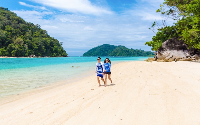 Tourists walking on the sandy beach at Chong Khad Bay with lush greenery and clear blue water.